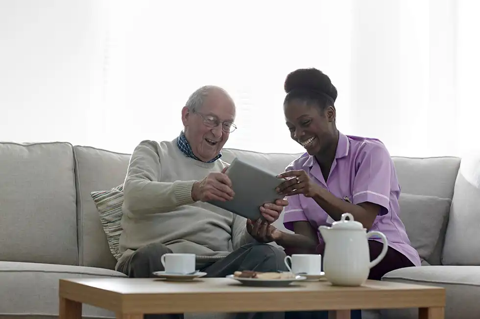 Man and carer looking at a tablet and laughing